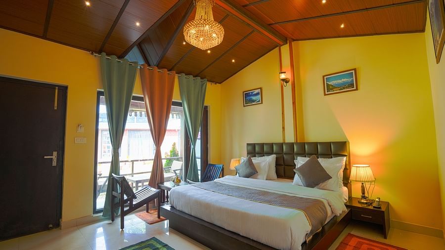 An image showing a large bed with cushions, bedside lamps, two chairs and a coffee table, and a chandelier